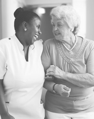 female healthcare worker holding hands with an elderly woman while taking a walk inside a healthcare facility